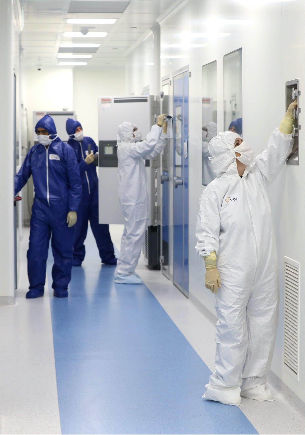 Lab technicians in blue and white lab hoodies, working in a white hallway at VBL’s production facility in Modiin, Israel.